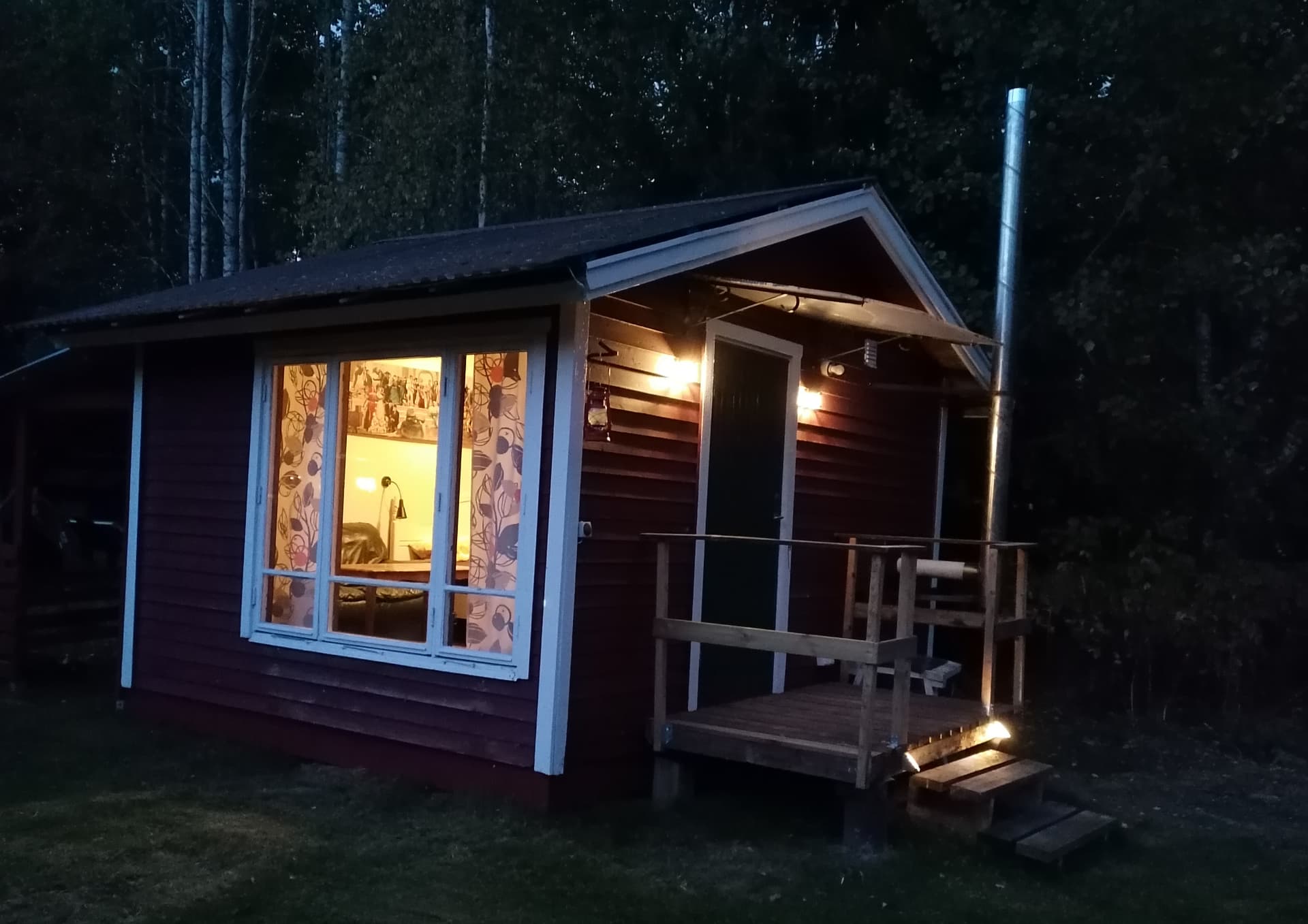 Stugan i kvällsljus med tända lampor