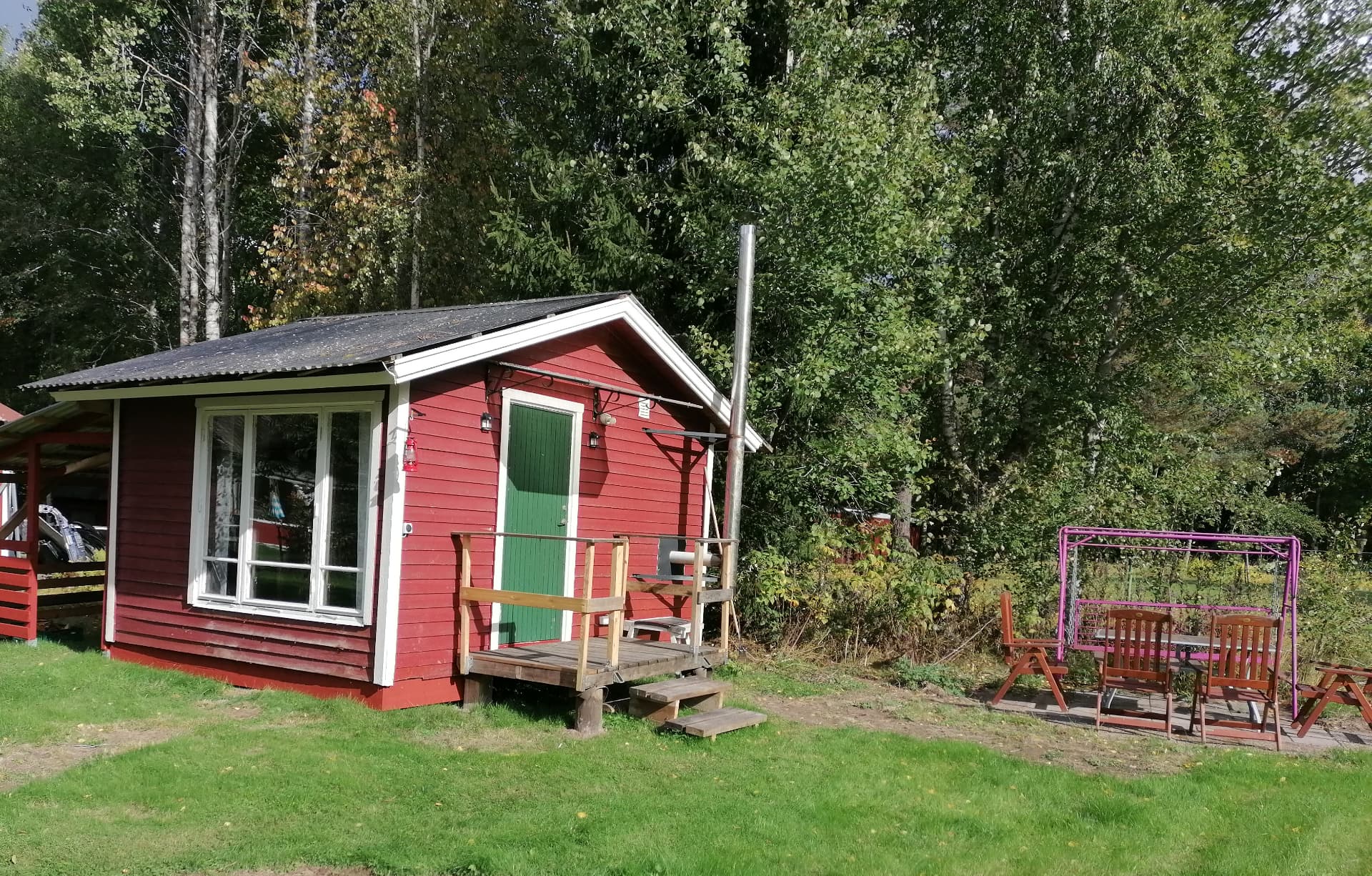 Röd trästuga med grön dörr och veranda i trädgården